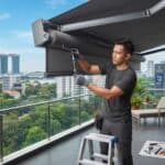 Professional awning repair technician tensioning replacement fabric on a residential balcony in Singapore